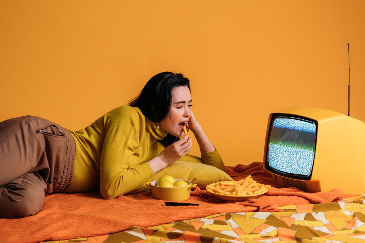 Woman dining on snacks while watching a vintage TV in a retro, colorful setting.